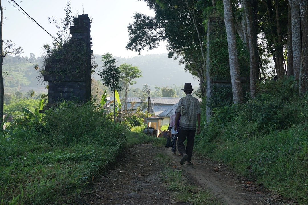 a man walking down a dirt road next to a forest